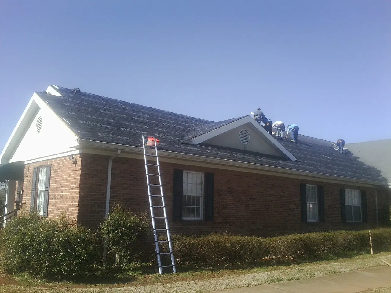 Crew tearing shingles off a brick ranch roof with a ladder set — Emergency Roof Repair work by our crew in Baker