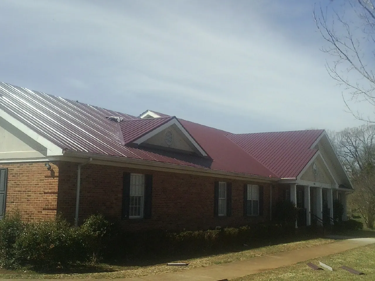 Red metal roof with gabled entries on a long brick building, from a Hail Damage Roof Repair job in Baker