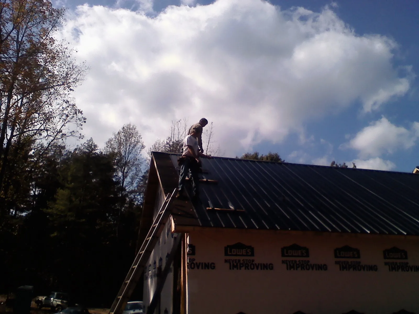 Roofer fastening dark metal panels high against a cloudy sky, from a Roof Inspection job in Baker